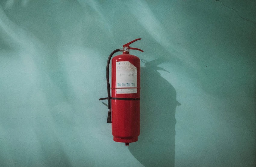 A fire extinguisher hanging on a teal-coloured wall.