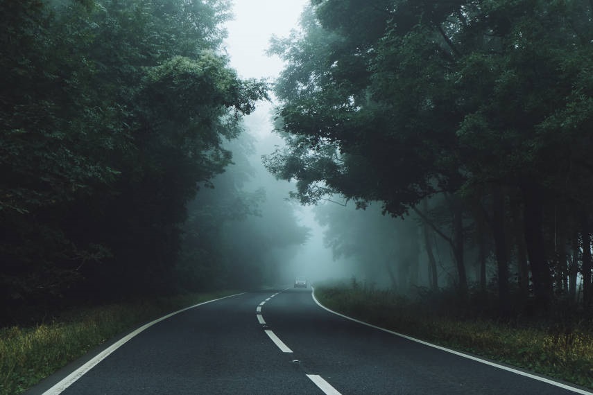 An image of a lonely vehicle travelling on a foggy road